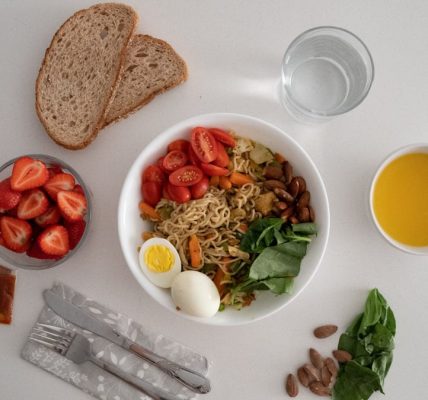 A balanced meal featuring a variety of healthy ingredients including noodles, eggs, almonds, strawberries, and fresh vegetables.