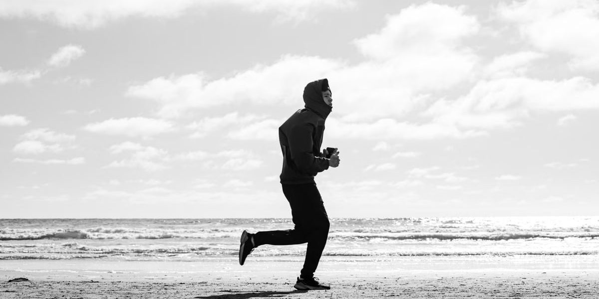 Silhouette of a jogger running along La Lucila del Mar beach, captured in monochrome.